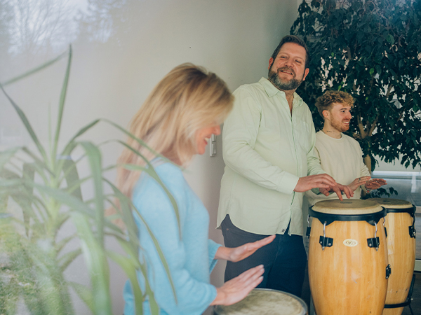 Drei Patienten spielen lachend Trommeln in der Musiktherapie