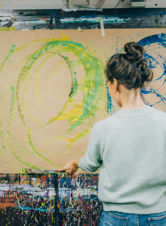 Frau steht vor ihrem in der Kunsttherapie selbst gemalten großen Gemälde