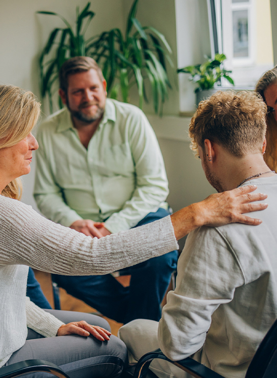 Eine Frau legt in einer Gruppentherapiesitzung einem jungen Mann unterstützend ihre Hand auf die Schulter