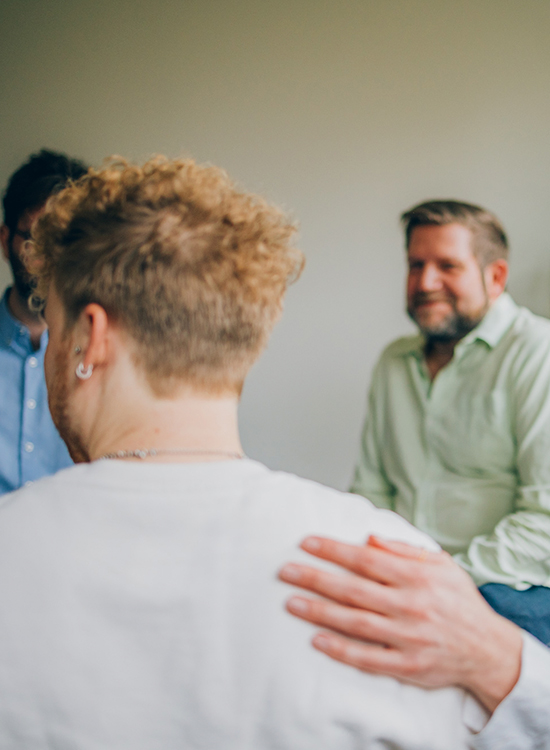 Mehrere männliche Personen sitzen in der Gruppentherapie im Stuhlkreis.