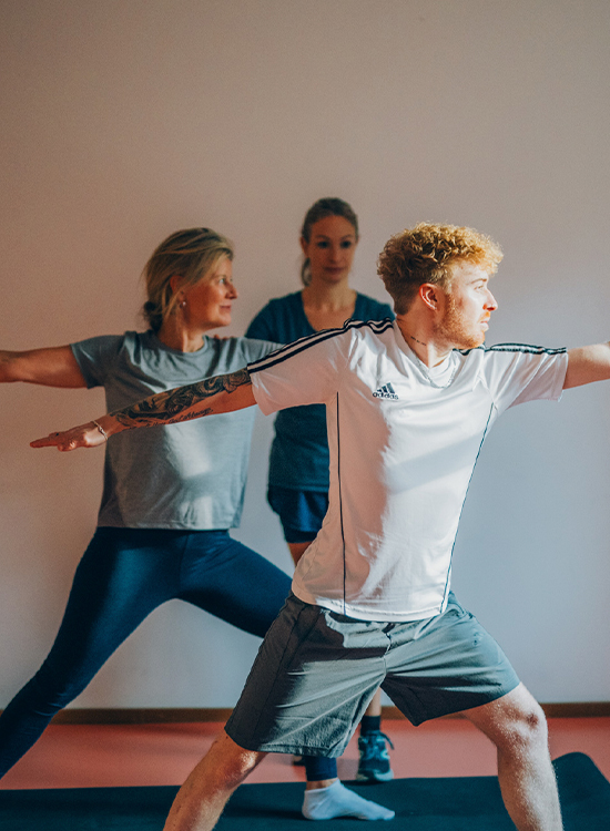 Eine Patientin und ein Patient machen unter Anleitung einer Therapeutin Yoga