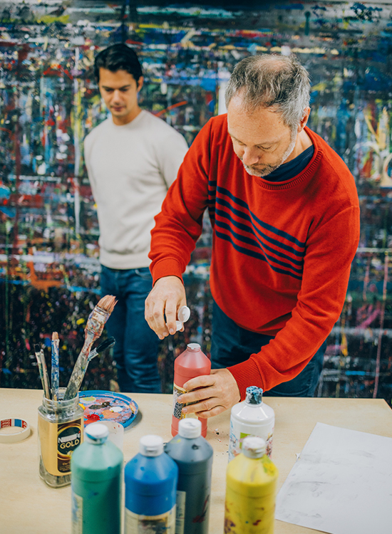 Ein Mann öffnet im Kunsttherapieraum eine Flasche roter Farbe