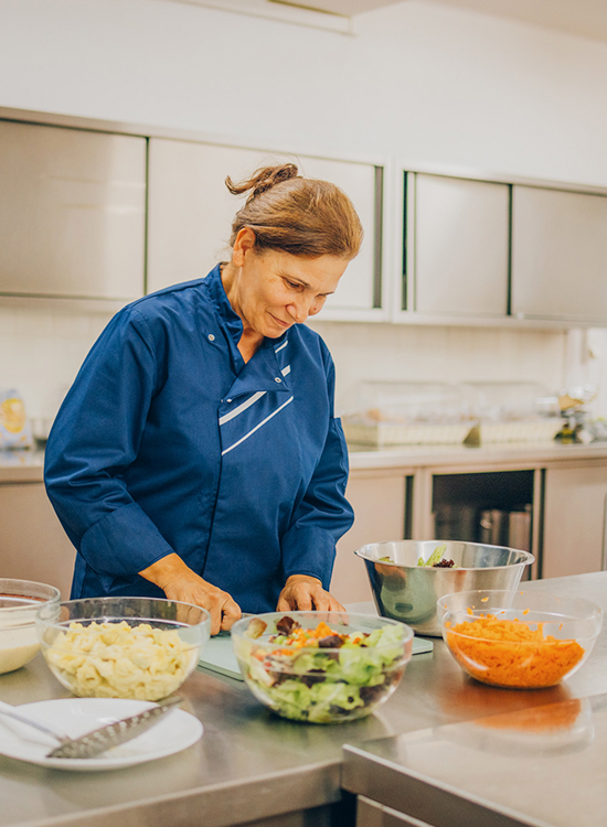 Eine Mitarbeiterin in blauer Kochkleidung bereitet in einer modernen Küche sorgfältig verschiedene frische Salate zu