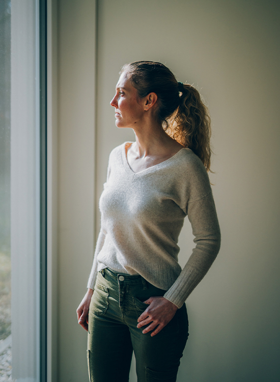 Eine Frau blickt nachdenklich aus dem Fenster, das sanftes Licht hereinlässt
